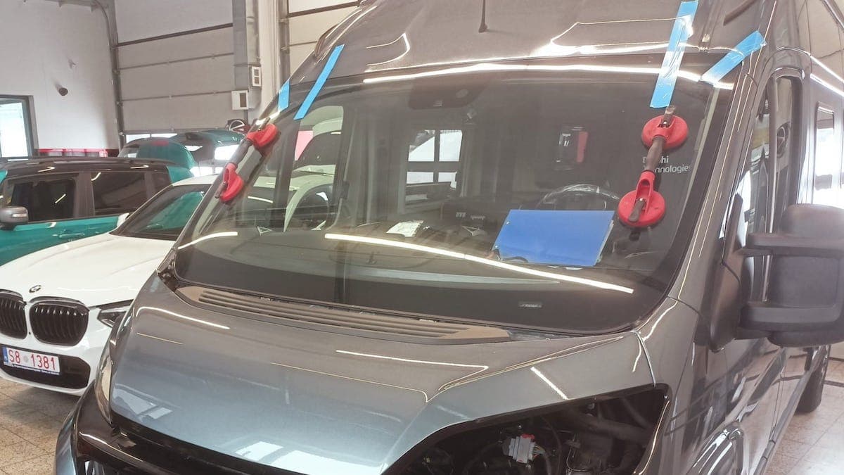 Wymiana szyby czołowej w samochodzie dostawczym. Samochód stoi w warsztacie, w tle inne samochody